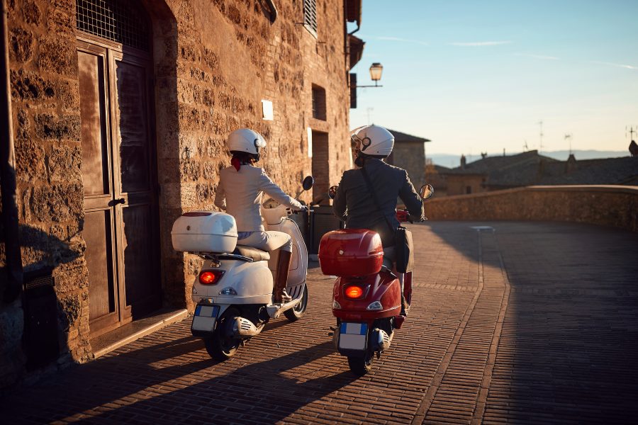 two people on vespas riding in the sunset in an ancient town of italy