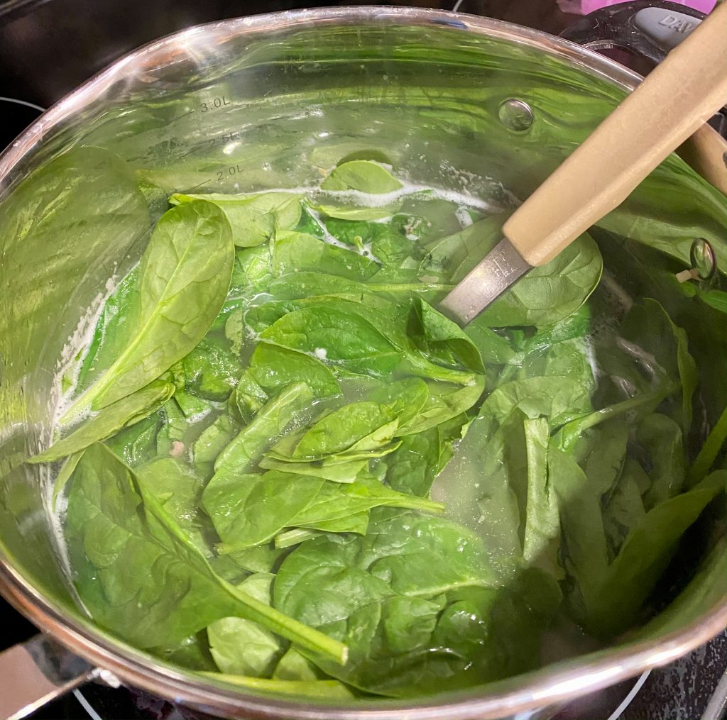 saucepan filled with soup and fresh spinach