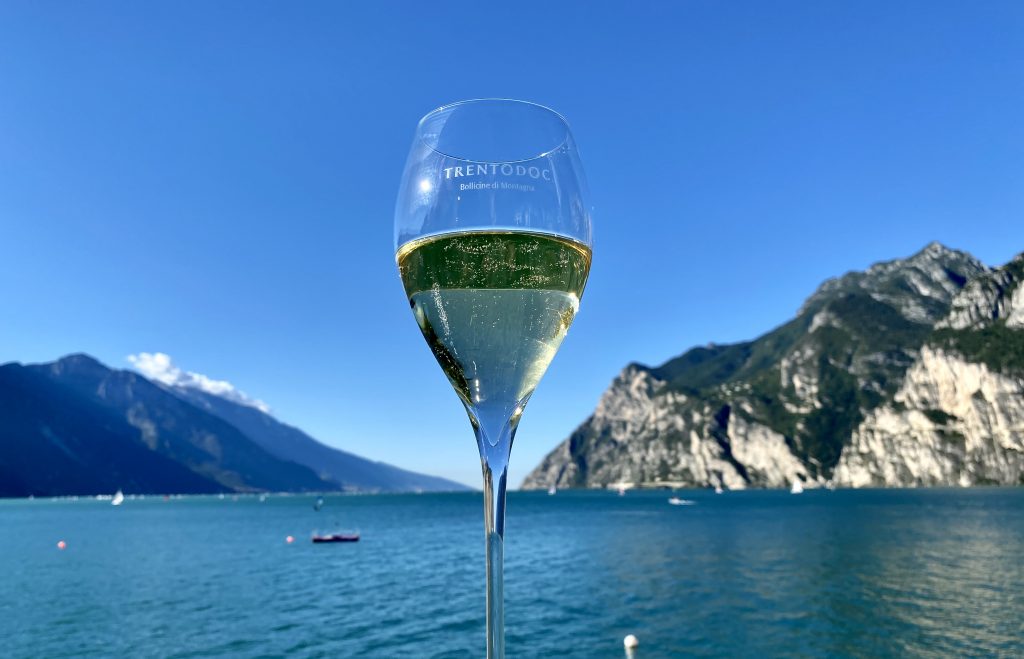 Trentodoc sparkling wine in glass in front of Lake Garda.