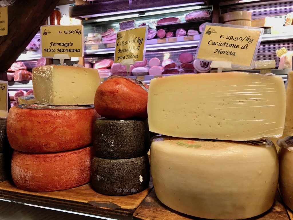 piles of cheese rounds; case of meats in background