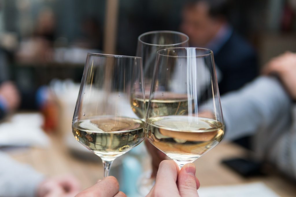 three hands toasting with white wine in glasses