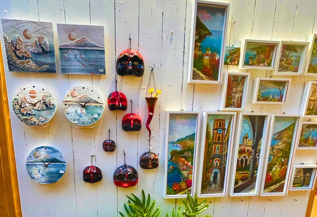 An outdoor display of colorful papier-mâché art from the shop Atmosfera in Sorrento, featuring traditional Pulcinella masks and red horn good luck charms, highlighting local crafts when exploring where to shop.