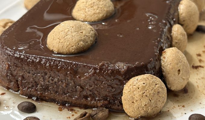 A slice of decadent Italian chocolate flan (bonet) with a thin caramel layer on top, garnished with amaretti cookies and coffee beans.