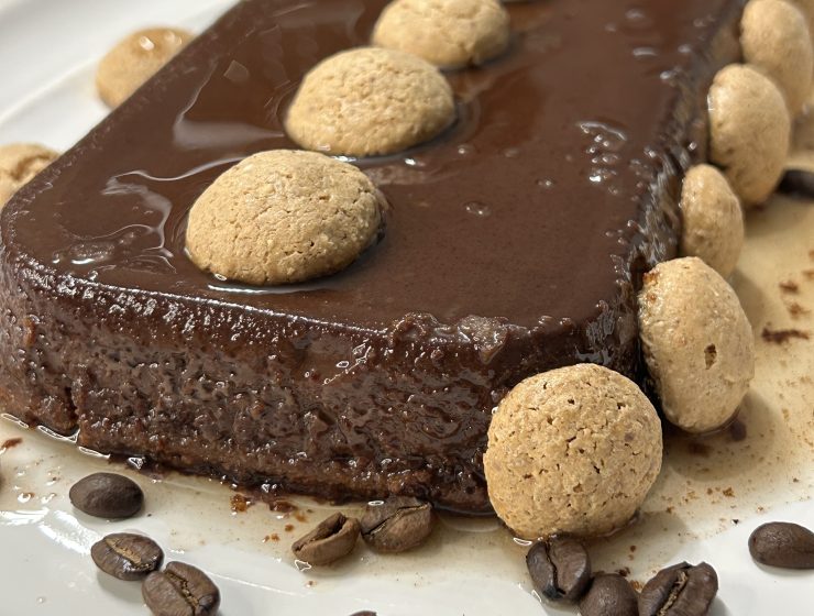 A slice of decadent Italian chocolate flan (bonet) with a thin caramel layer on top, garnished with amaretti cookies and coffee beans.
