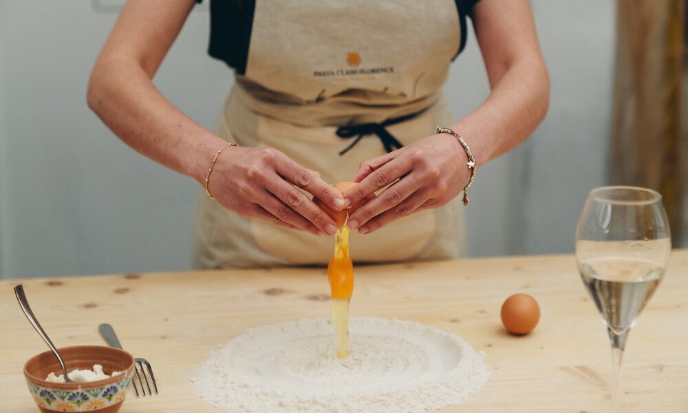 woman adding egg to flour to make fresh pasta
