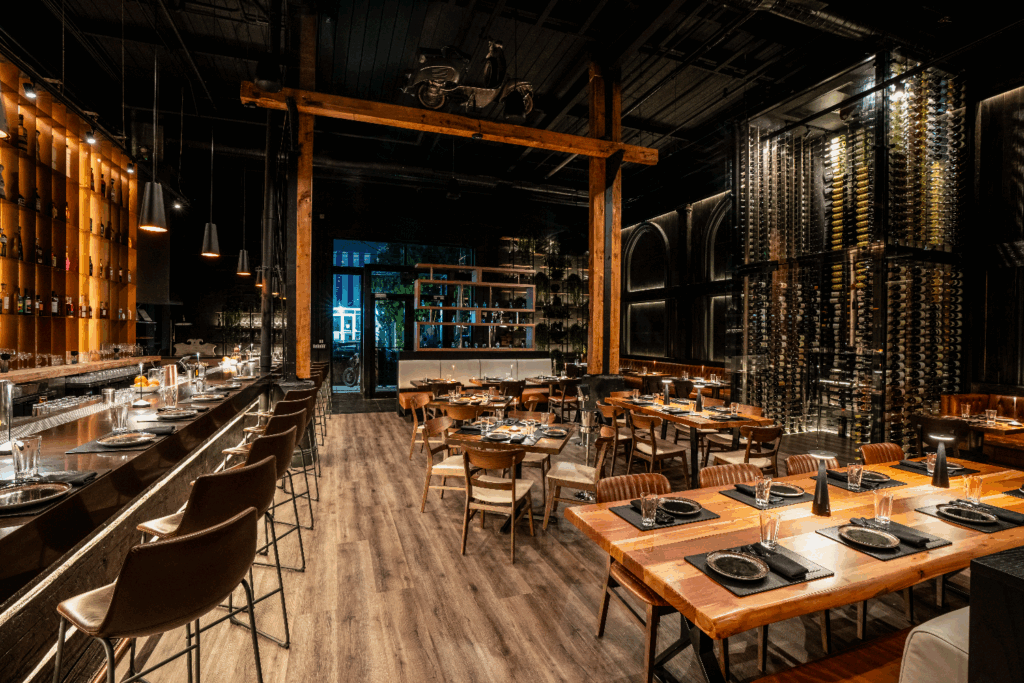 The restaurant features a sophisticated and moody ambience with dark wood and black finishes.