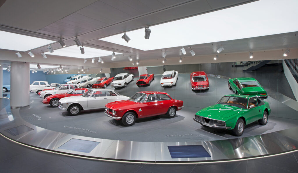 A row of vintage Alfa Romeo cars in green, white, and red at the museum.