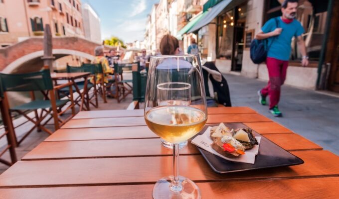 VENICE, ITALY: Wineglass and local Cichetti snacks in Venice, with historical bridges, restaurants and tourists on 29 September 2021. Ancient italian city and lagoon are UNESCO World Heritage Sites