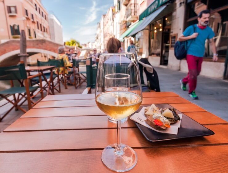 VENICE, ITALY: Wineglass and local Cichetti snacks in Venice, with historical bridges, restaurants and tourists on 29 September 2021. Ancient italian city and lagoon are UNESCO World Heritage Sites