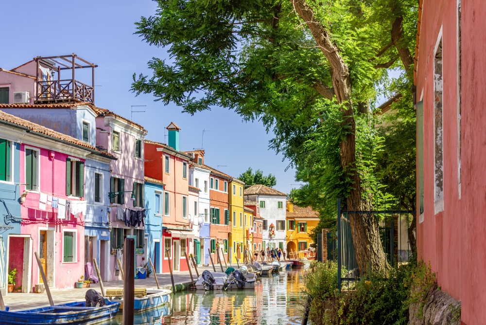Burano, Venice, Italy - June 17, 2025: Vibrant colorful houses and small boats along a peaceful canal on the charming island of Burano, Italy.