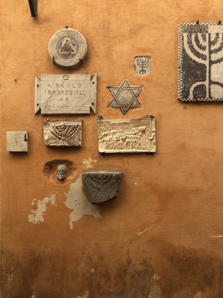 Historic Jewish Quarter in Rome featuring cultural symbols and architectural details along an ochre-coloured wall.