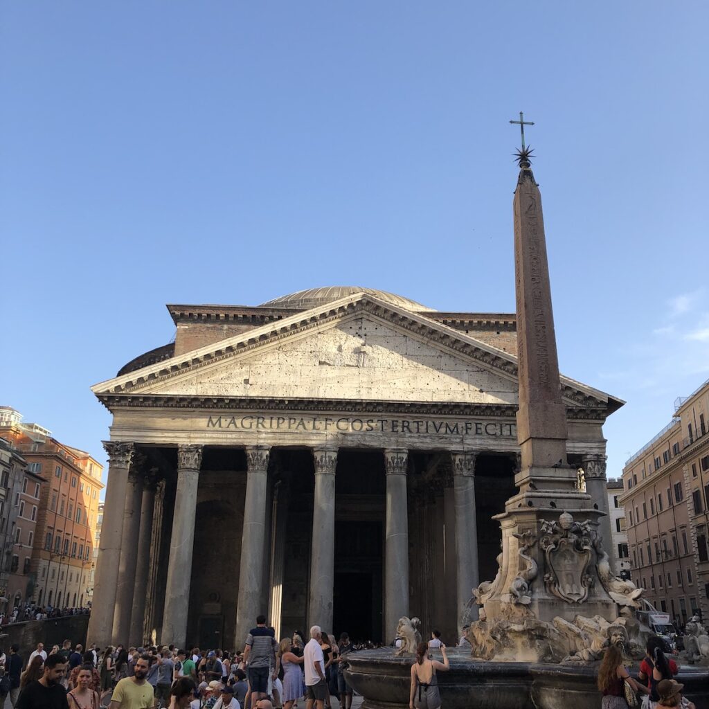 The Pantheon in Rome illuminated by afternoon light, with visitors gathered in Piazza della Rotonda.