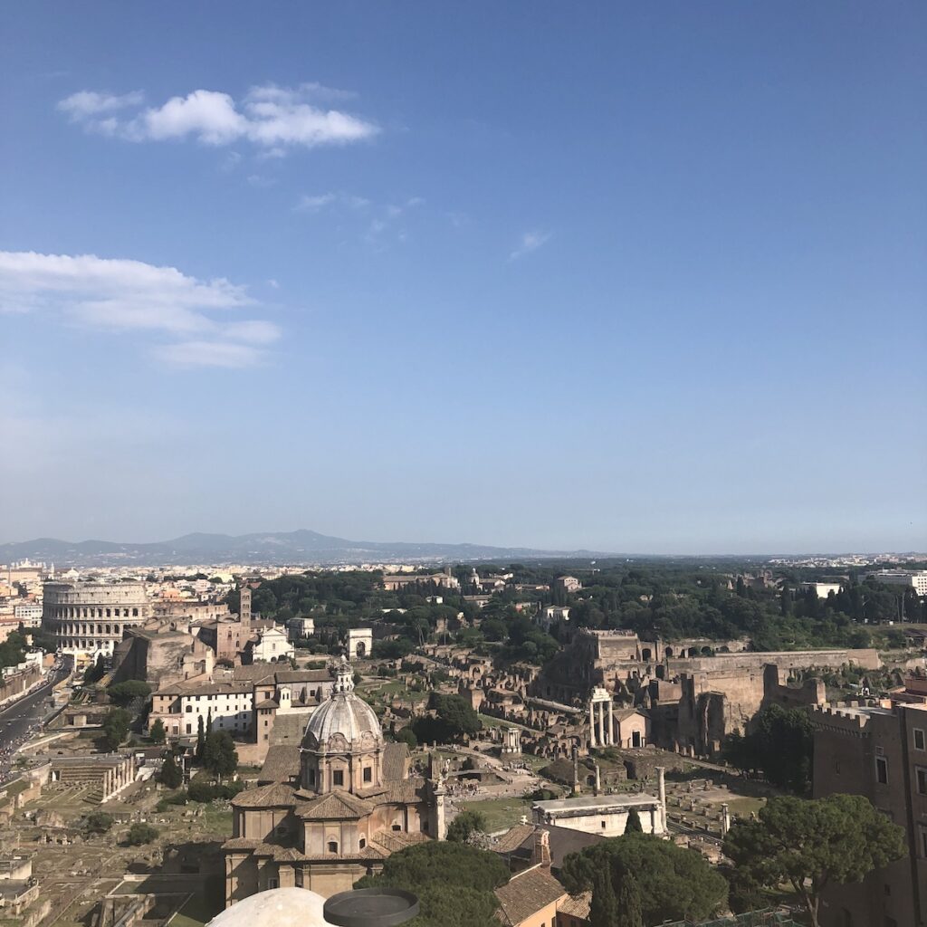 Panoramic view of Rome from above, overlooking the Roman Forum, historic churches, and the Colosseum.
