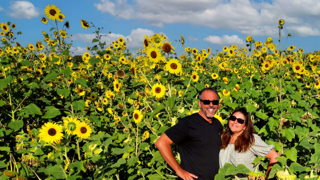 Sandy and Phil Ferretti standing amongst tall, blooming sunflowers in a vibrant field, showcasing a typical and authentic scene of Tuscan agriculture.