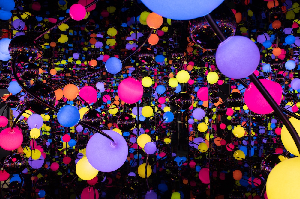 Yayoi Kusama's Infinity Mirrored Room installation featuring colorful illuminated spheres reflected infinitely in mirrors at OGR Torino.