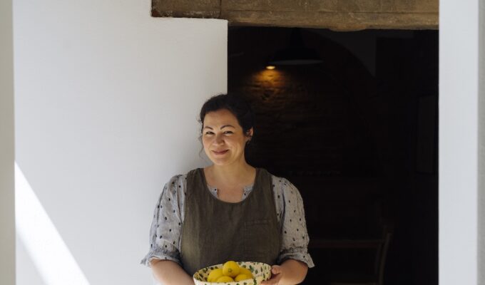 Emiko Davies holding a ceramic bowl of fresh lemons in a rustic Tuscan interior.
