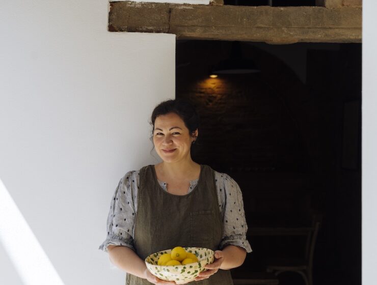 Emiko Davies holding a ceramic bowl of fresh lemons in a rustic Tuscan interior.