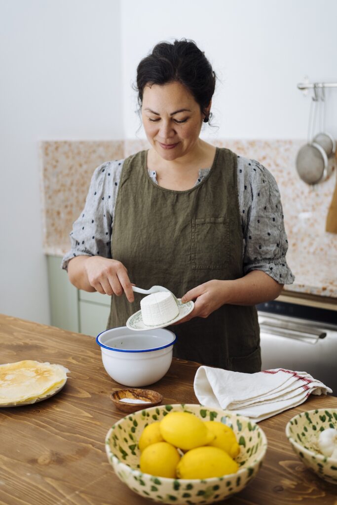 Cookbook author Emiko Davies preparing fresh ricotta in her kitchen, with lemons and traditional ingredients on the table.