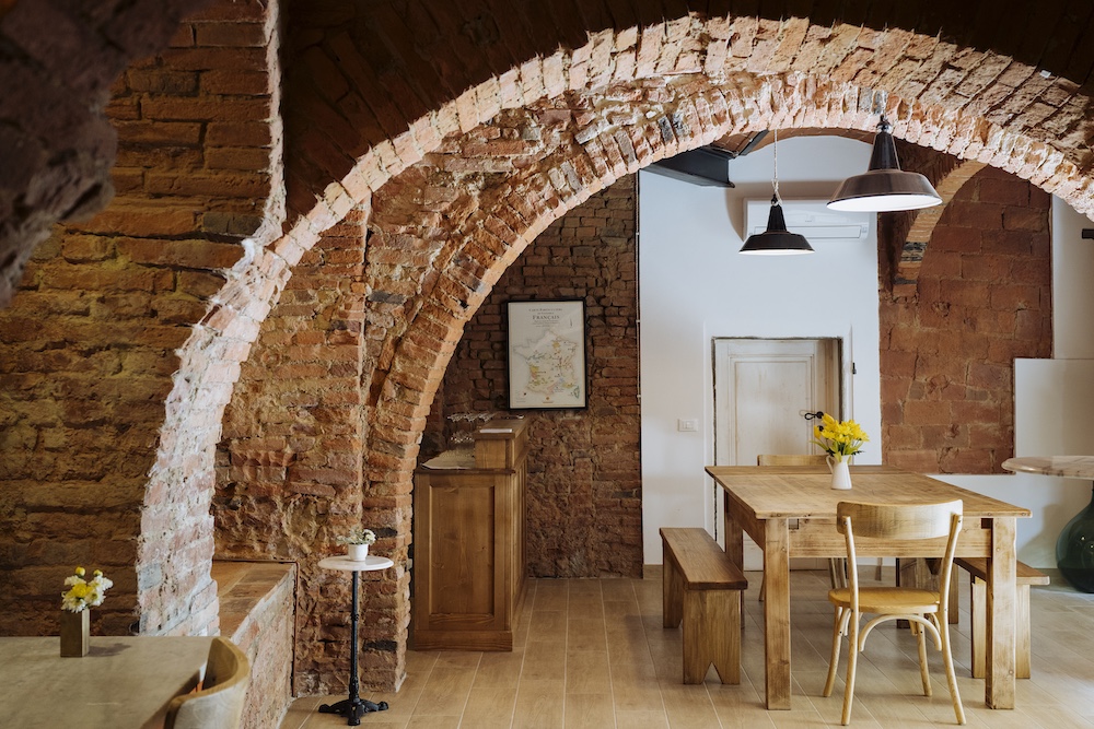 Rustic interior of Enoteca Marilu in San Miniato, Tuscany, featuring exposed brick arches and wooden tables.