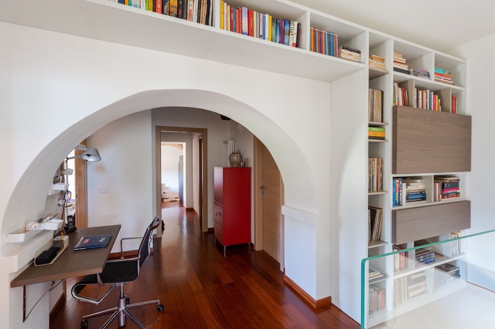 Second-floor home office and library with built-in bookshelves, wooden floors and an arched doorway inside a restored Tuscan abbey residence.