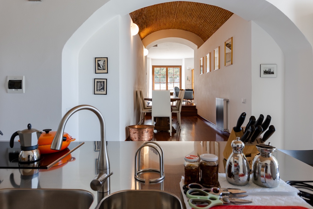 Modern kitchen overlooking the dining area beneath an arched brick ceiling in a restored historic abbey residence in Tuscany.