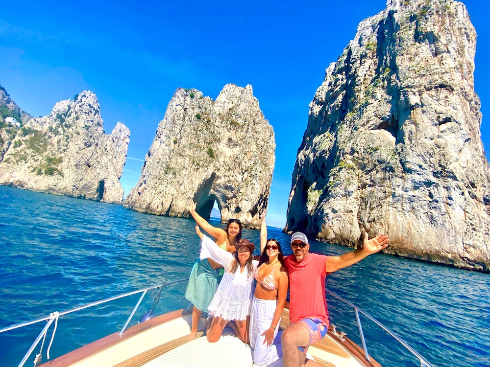 Four travelers enjoying a private boat excursion near Capri's famous Faraglioni rock formations in the Mediterranean Sea.
