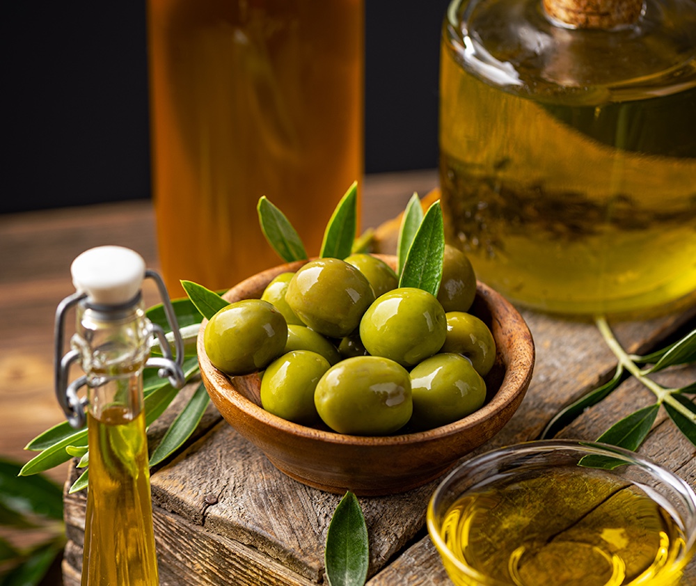 Extra virgin olive oil in a glass bottle surrounded by fresh olives.