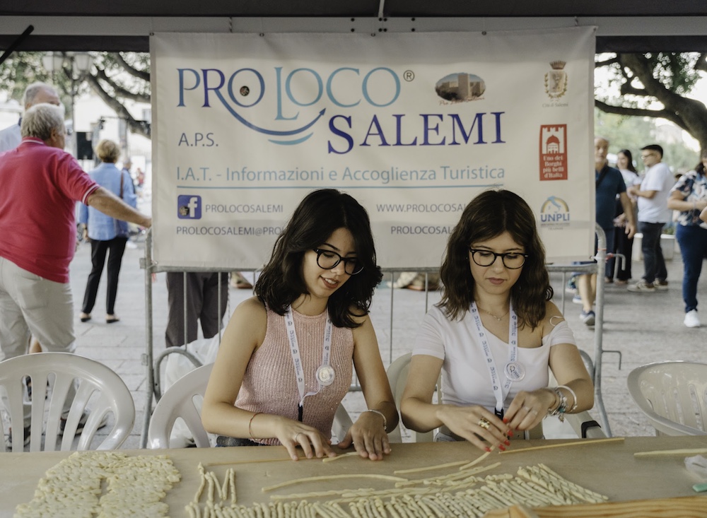 Two women learning to shape traditional Sicilian busiata pasta by hand at a Pro Loco workshop in Salemi.
