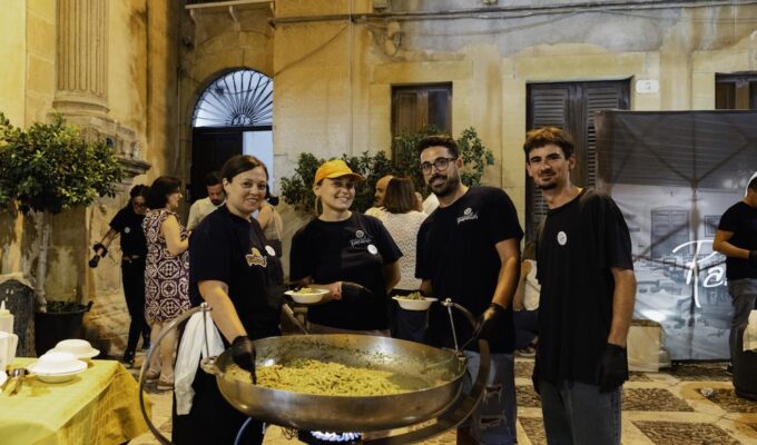 Festival food vendors gathered around a large pan of freshly prepared busiata pasta in Salemi's historic center during the Sagra della Busiata in Sicily.