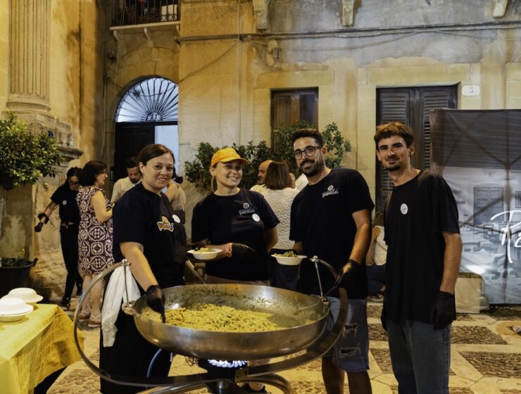 Festival food vendors gathered around a large pan of freshly prepared busiata pasta in Salemi's historic center during the Sagra della Busiata in Sicily.