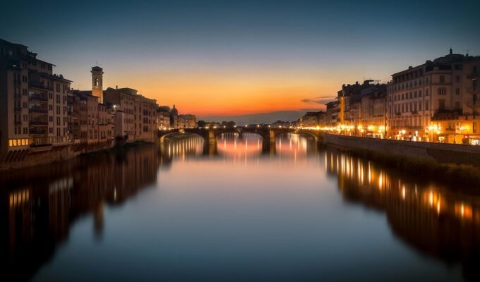 Florence at sunset with illuminated bridges reflecting on the Arno River, Italy.