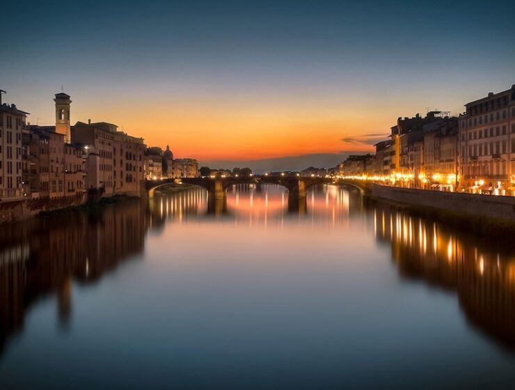 Florence at sunset with illuminated bridges reflecting on the Arno River, Italy.