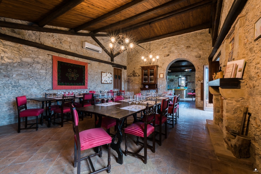 Rustic wine tasting room with stone walls, wooden ceiling and red upholstered chairs at Librandi winery.