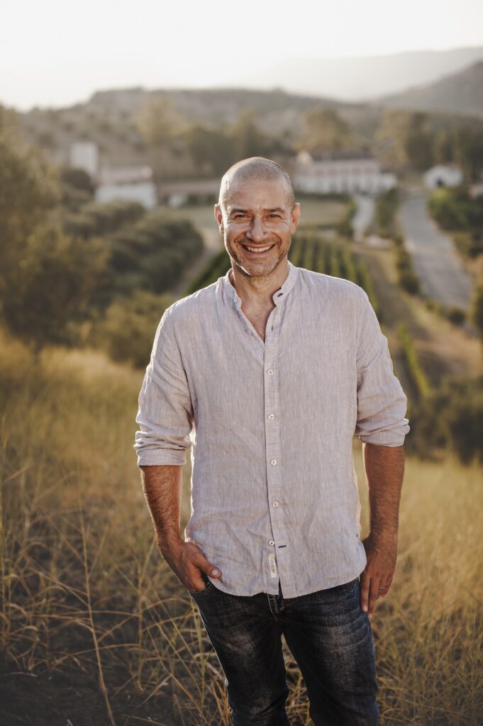 Paolo Librandi standing outdoors with vineyards and the Calabrian countryside behind him.
